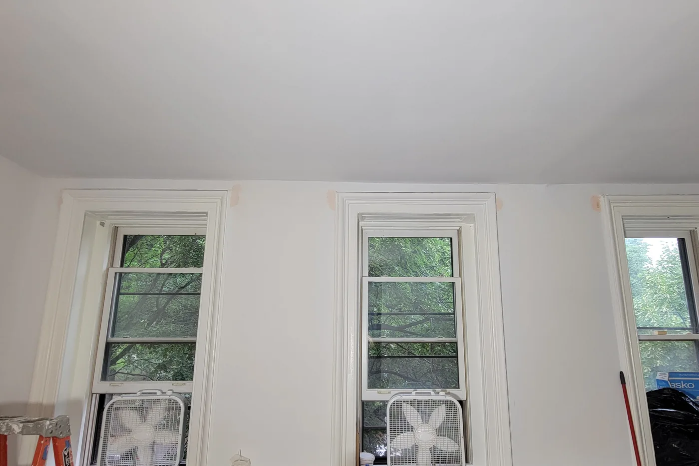 The same parlor before painting: flat white walls with patched, unpainted repairs above the window heads.