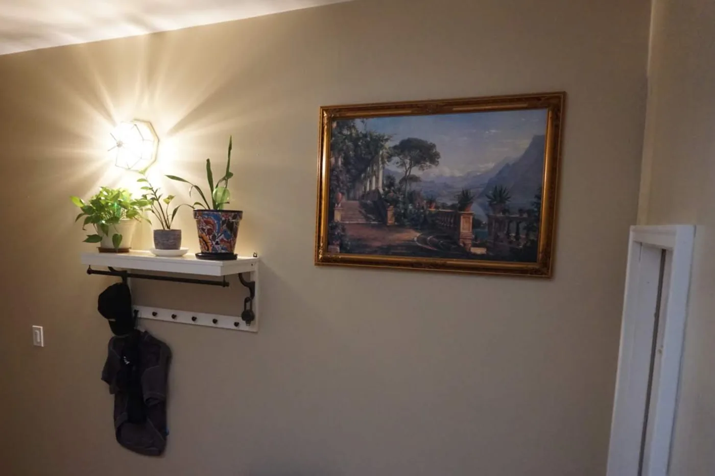 An entry wall after a patch repair and painting: one even warm gray, the shelf and framed picture back up, no patch left showing.